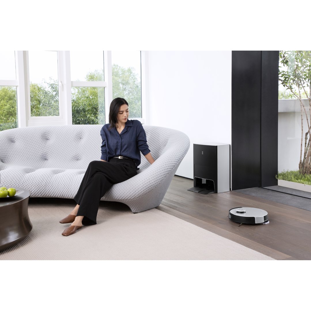 Woman sitting on a sofa while a robotic vacuum cleans the floor
