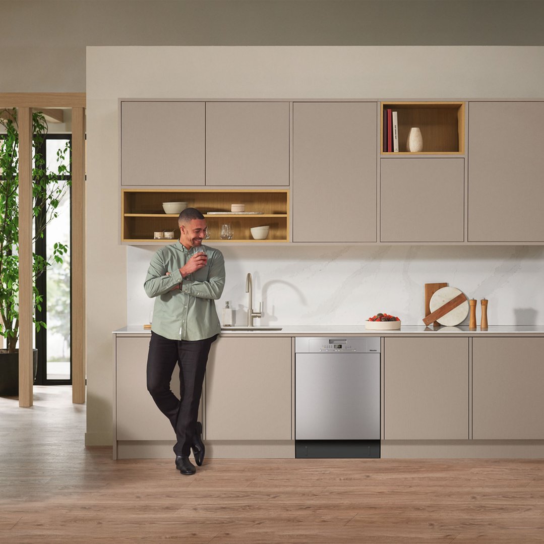 Man leaning on kitchen counter with a Miele dishwasher in a modern kitchen