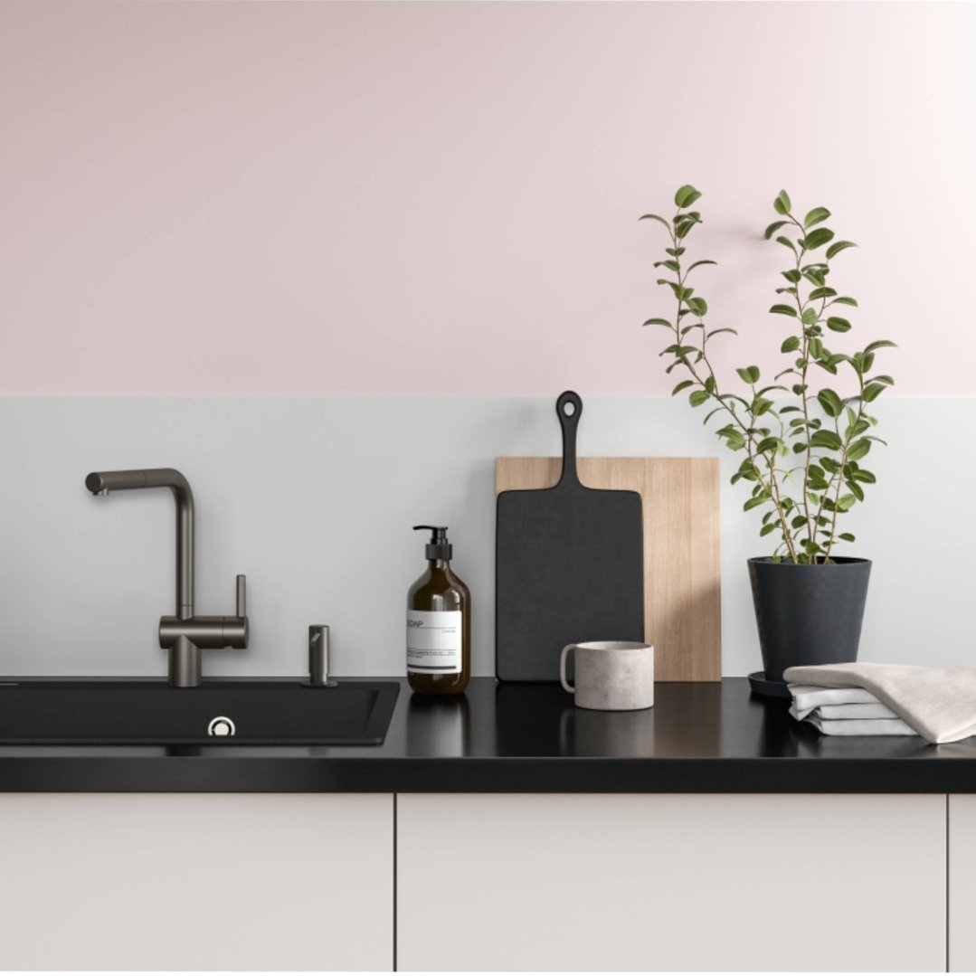 Gun metal mixer tap in a kitchen sink with plants and cutting boards