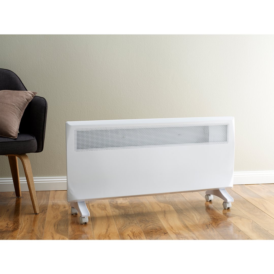 White electric panel heater on wheels on a wooden floor next to a chair