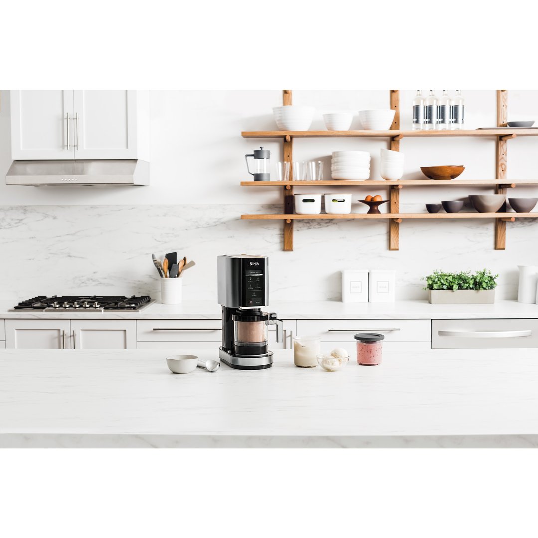 Ninja CREAMi ice cream maker on a kitchen counter with ingredients and bowls