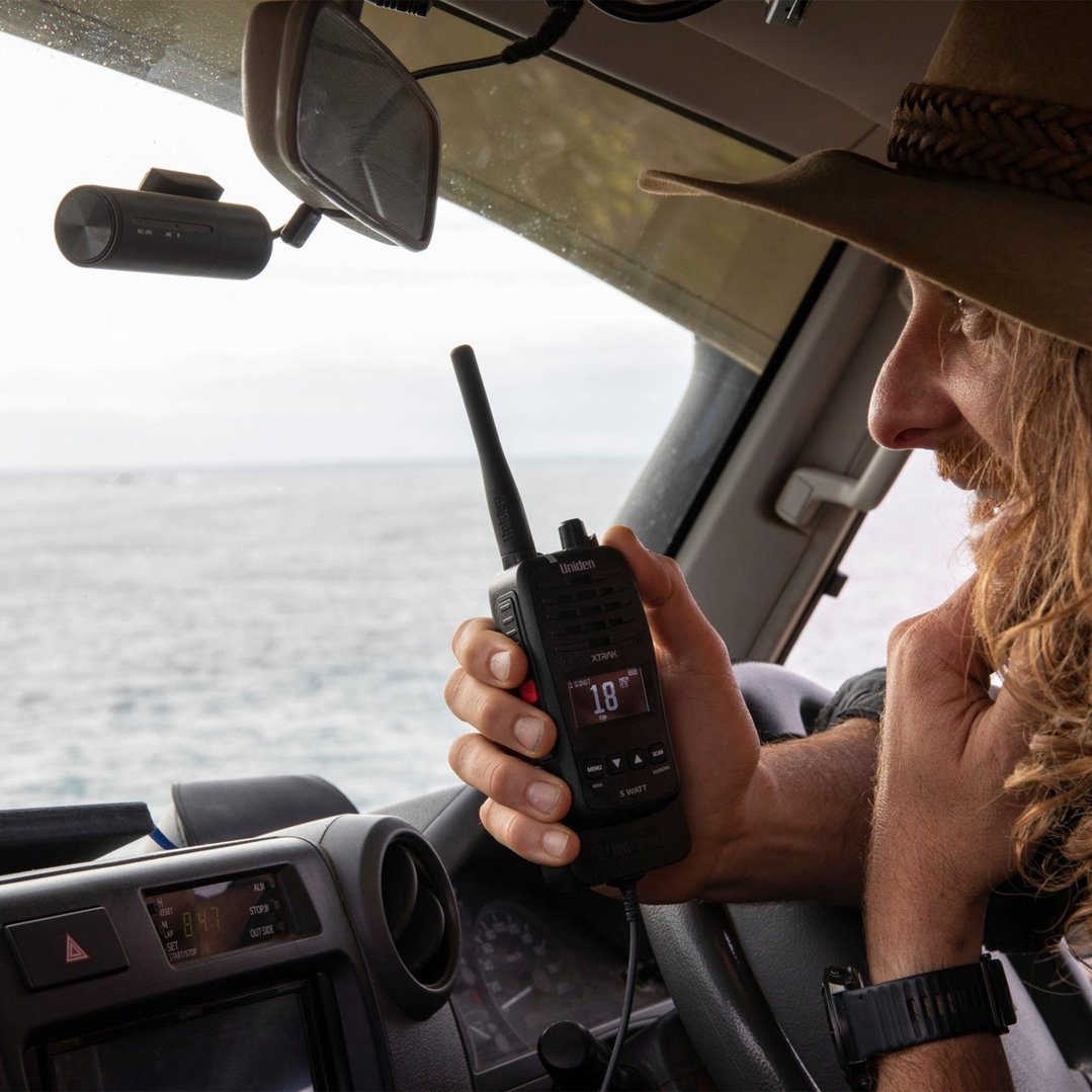 Man in a car holding a Uniden 5 Watt Waterproof Smart UHF Handheld Radio