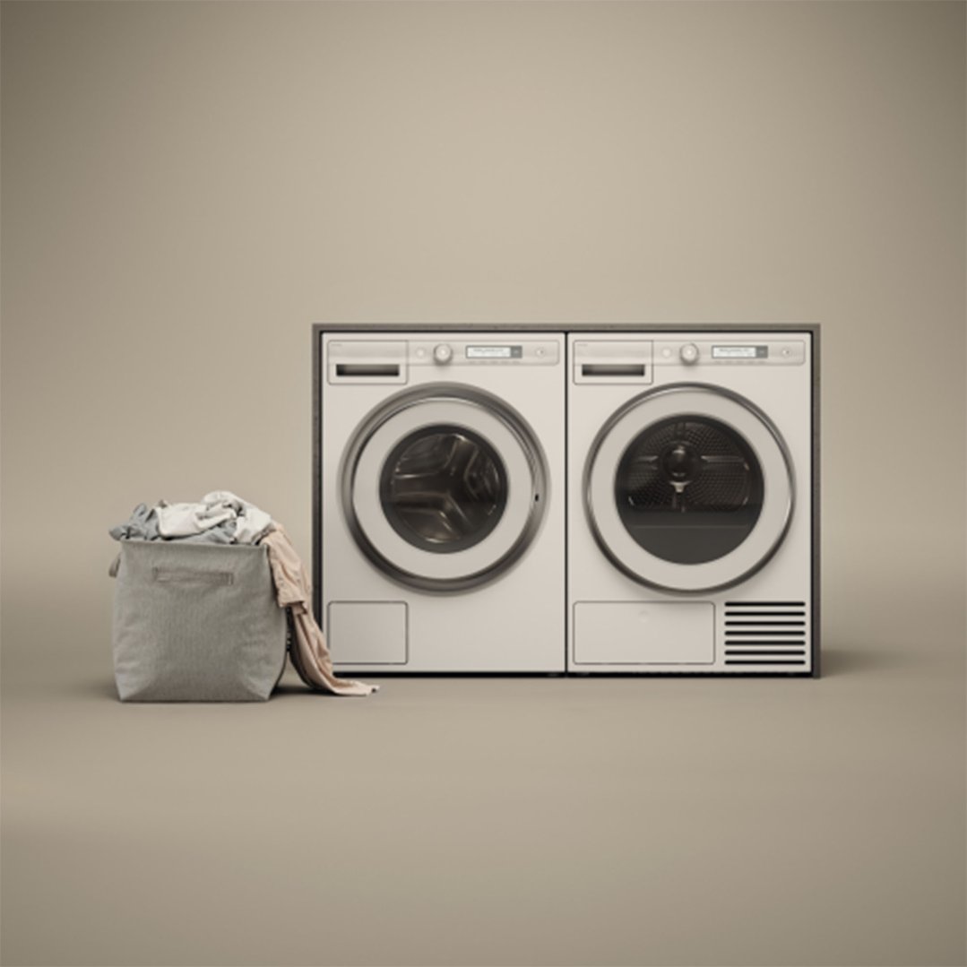 Two white washing machines side-by-side with a laundry basket of clothes