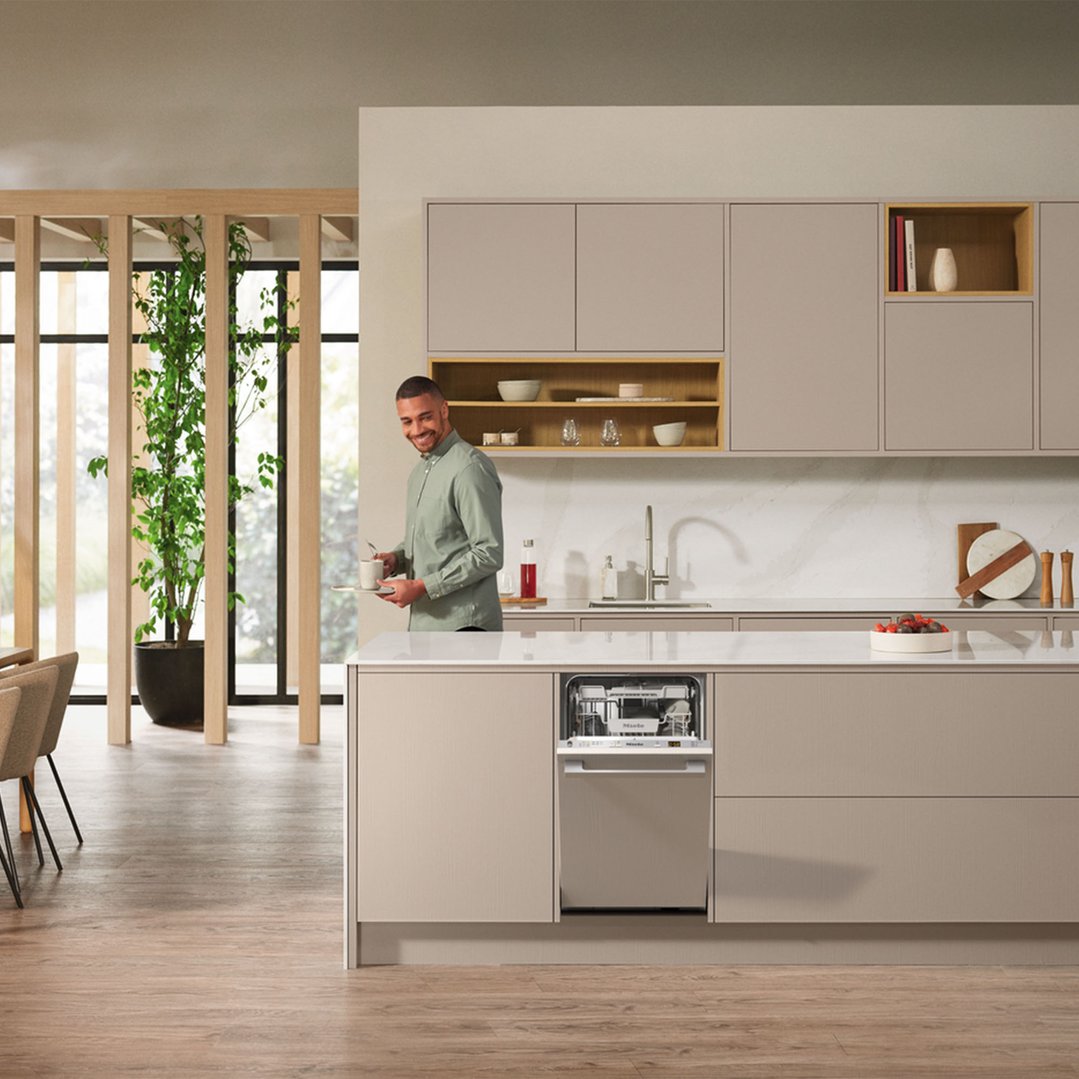 Man holding a mug and tray in a modern kitchen with an open dishwasher