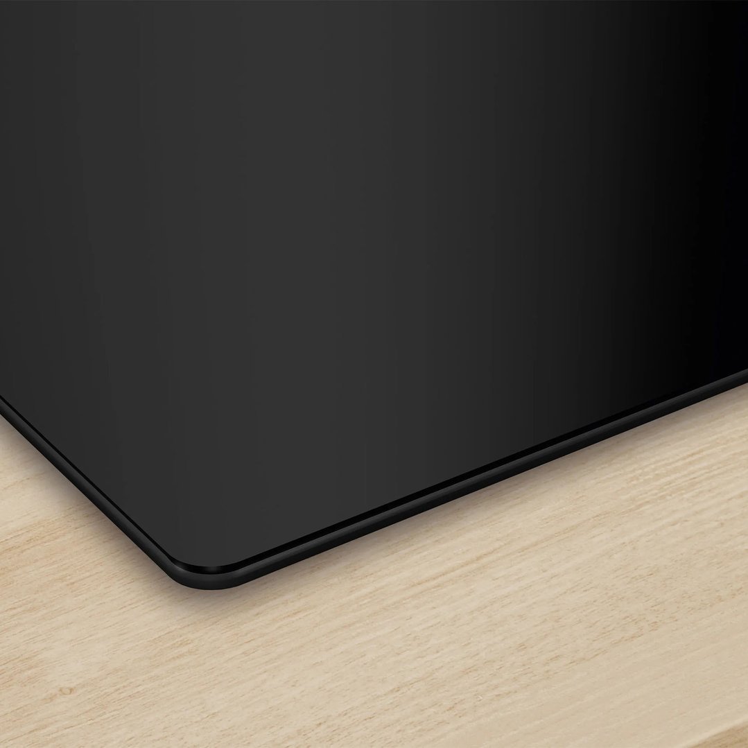 Black induction cooktop with rounded corners on a light wooden countertop