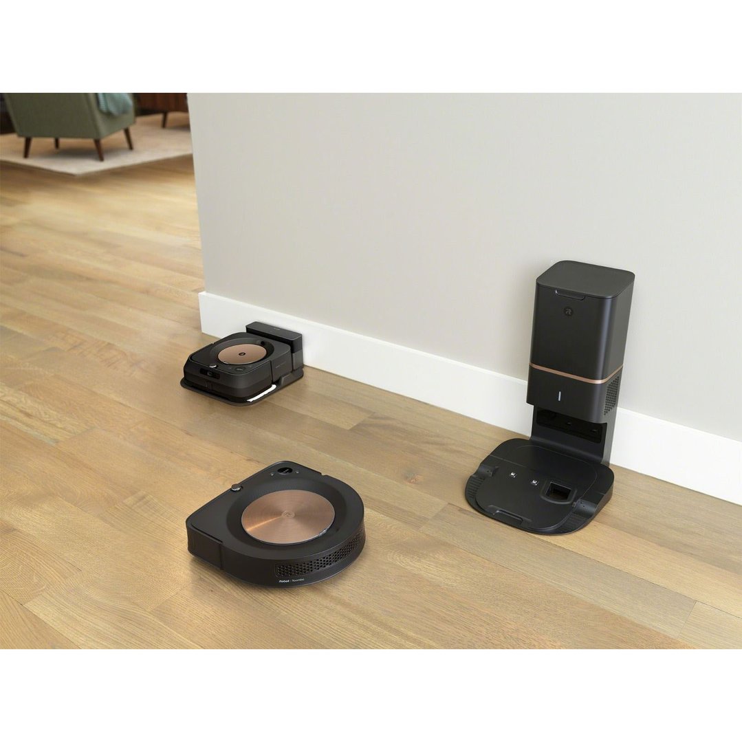 Three black robot vacuum cleaners and their charging stations on a wooden floor