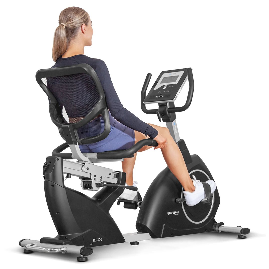 Woman exercising on a recumbent bike, viewed from behind and slightly to the side