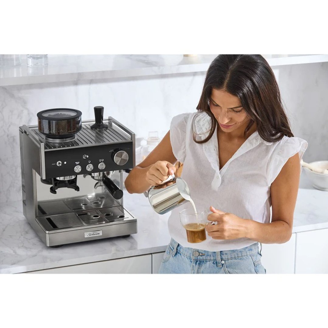 Woman pouring frothed milk into a glass of coffee from a Sunbeam espresso coffee machine