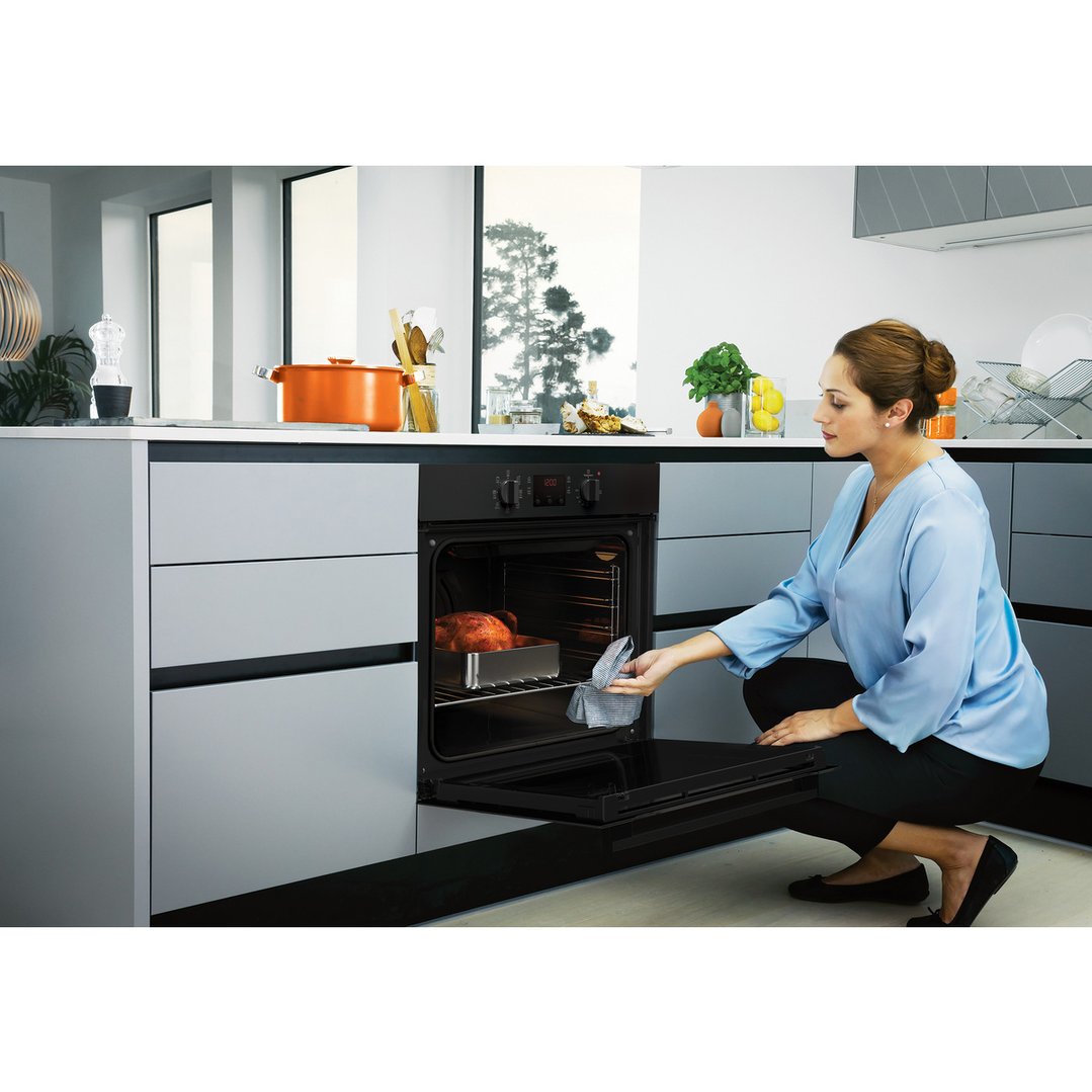 Woman checking a roasted chicken in a built-in oven in a modern kitchen