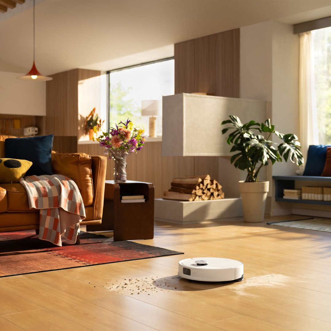 Robotic vacuum cleaner cleaning a messy wooden floor in a sunlit living room