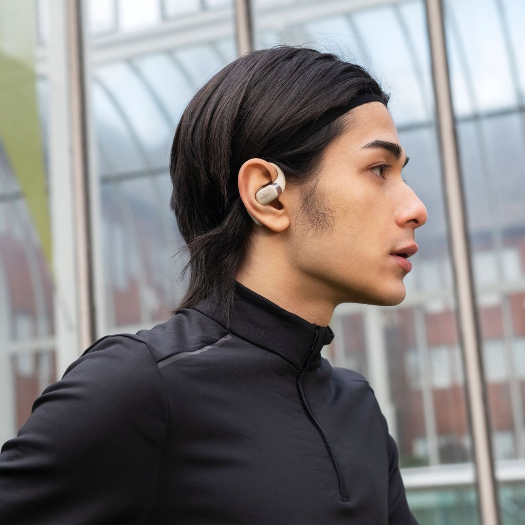 Man wearing beige Shokz OpenFit headphones in an outdoor setting