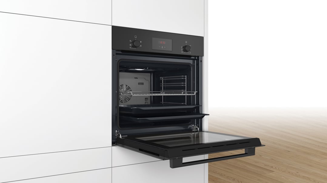 Built-in oven with door open, showing interior racks and trays in a kitchen