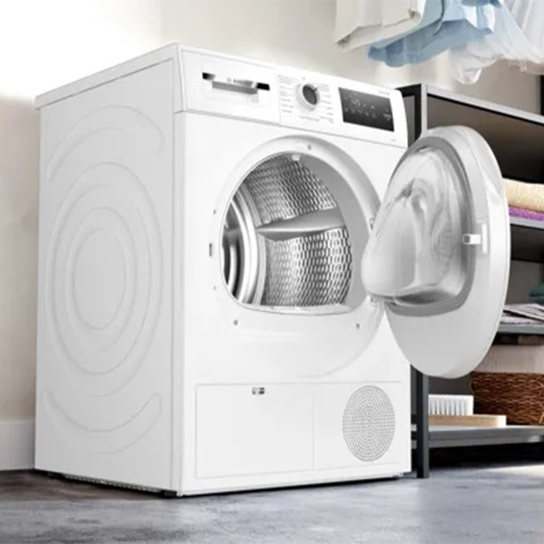White Bosch heat pump tumble dryer with door open in a laundry setting
