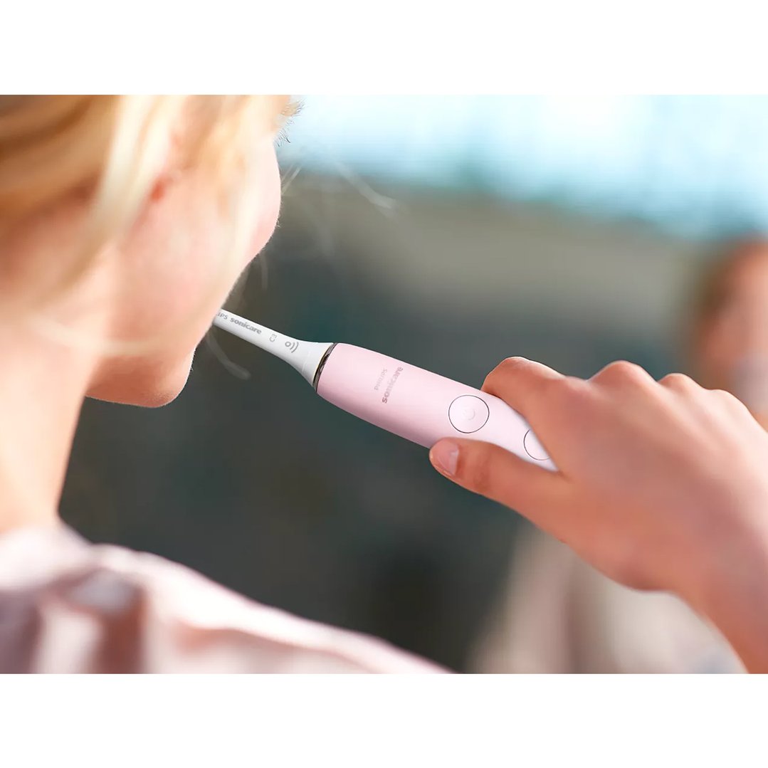 Person holding a pink electric toothbrush to their mouth