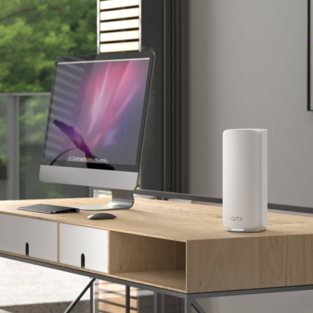 Orbi 870 Series WiFi 7 Mesh router on a wooden desk with a computer