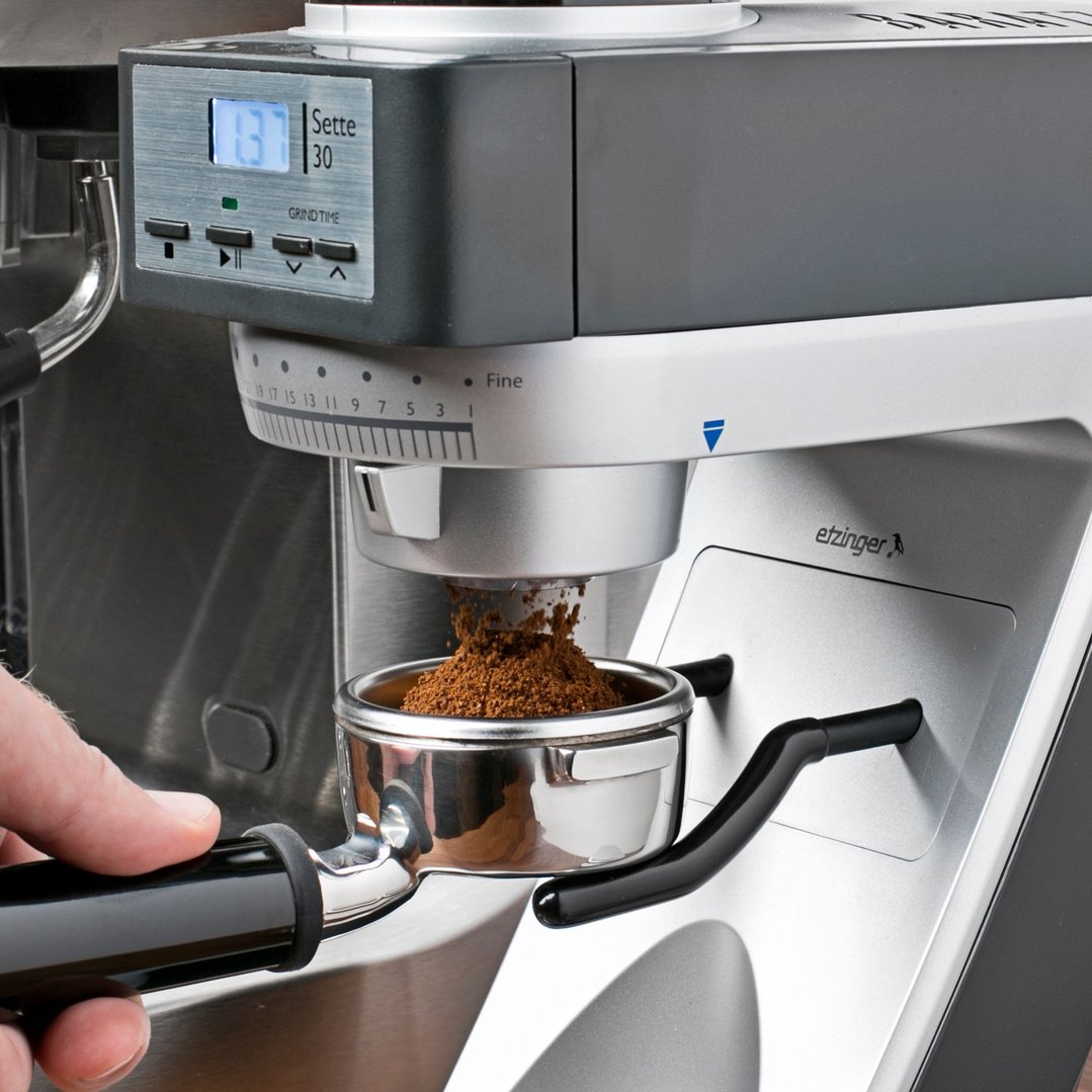 Hand holding a portafilter under a coffee grinder dispensing ground coffee