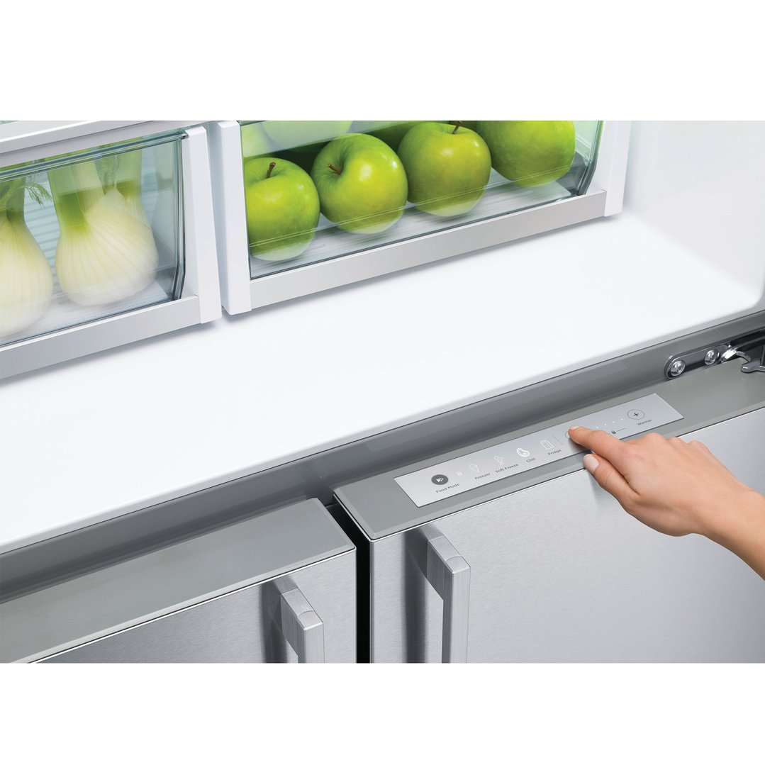 Hand pressing controls on a stainless steel refrigerator with fresh produce inside