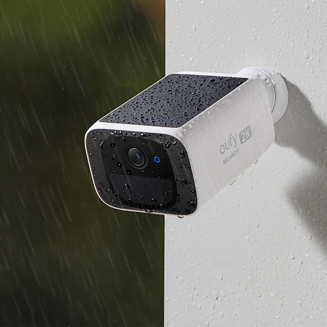 Security camera with solar panel on top, covered in raindrops, mounted outdoors