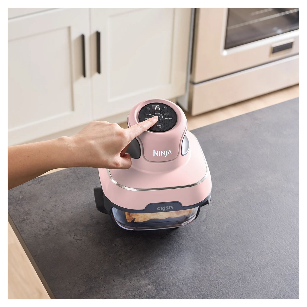 Hand pressing buttons on a pink Ninja Crispi air fryer on a countertop