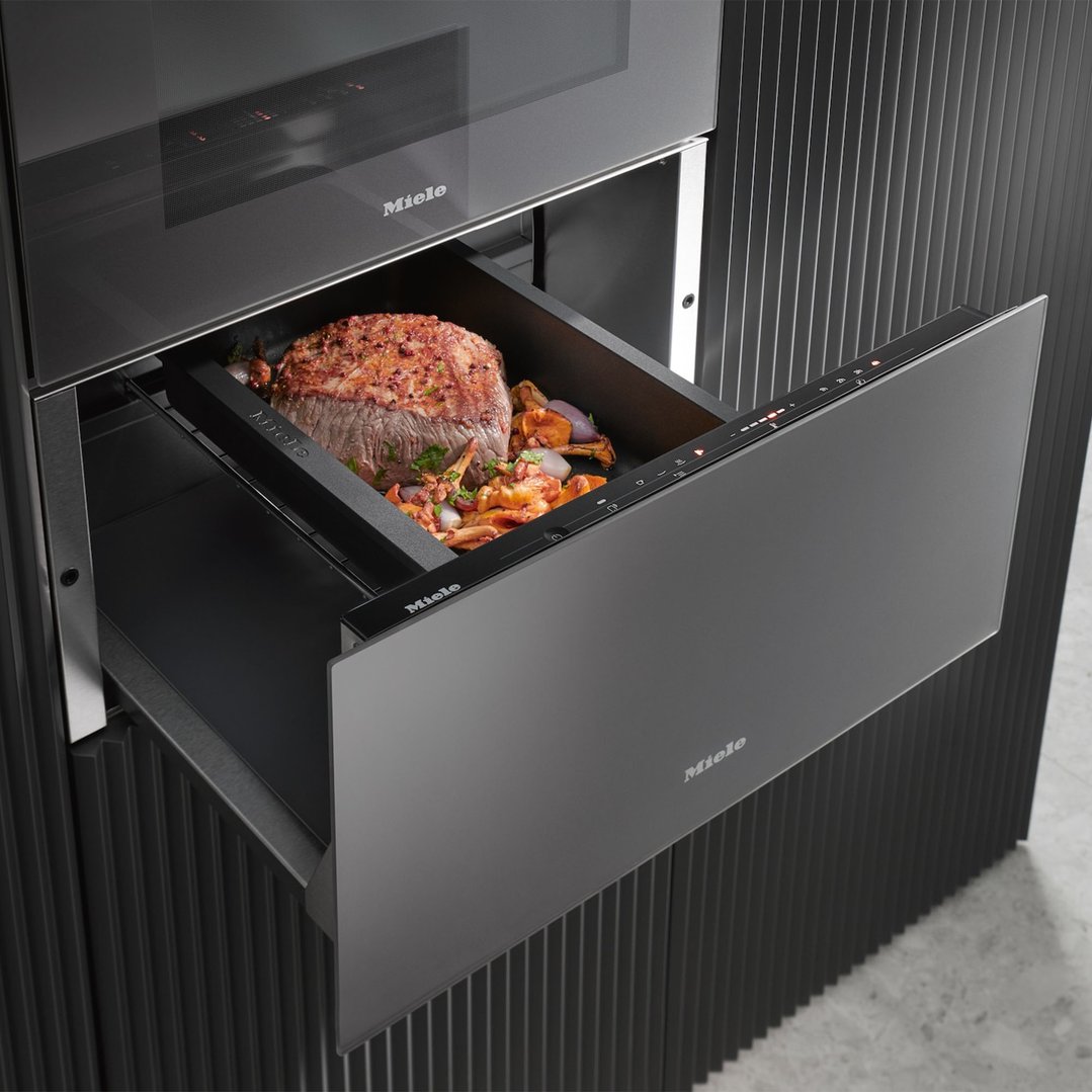 Open warming drawer with cooked meat and vegetables inside