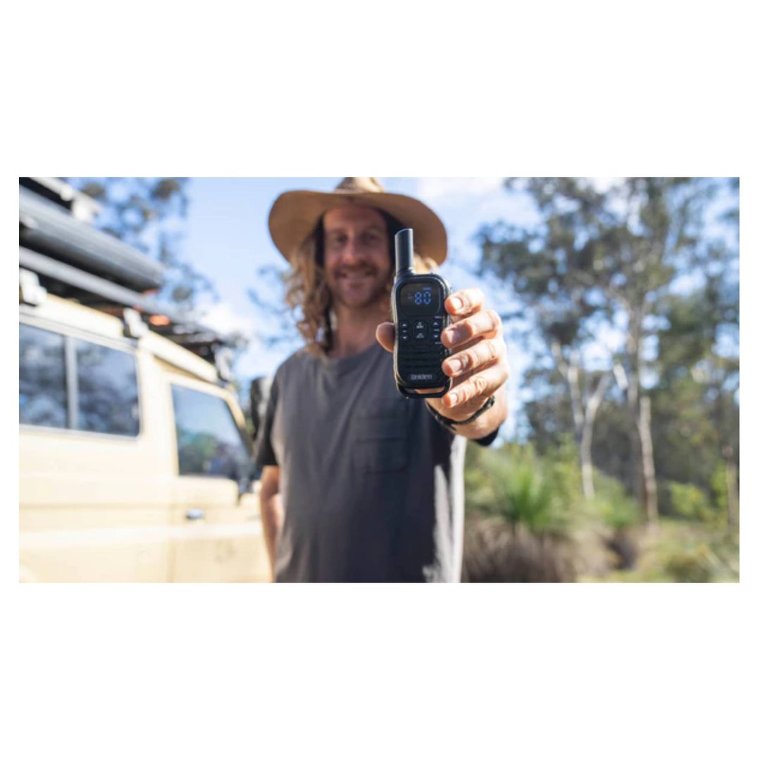 Man in a hat holding up a black two-way radio outdoors