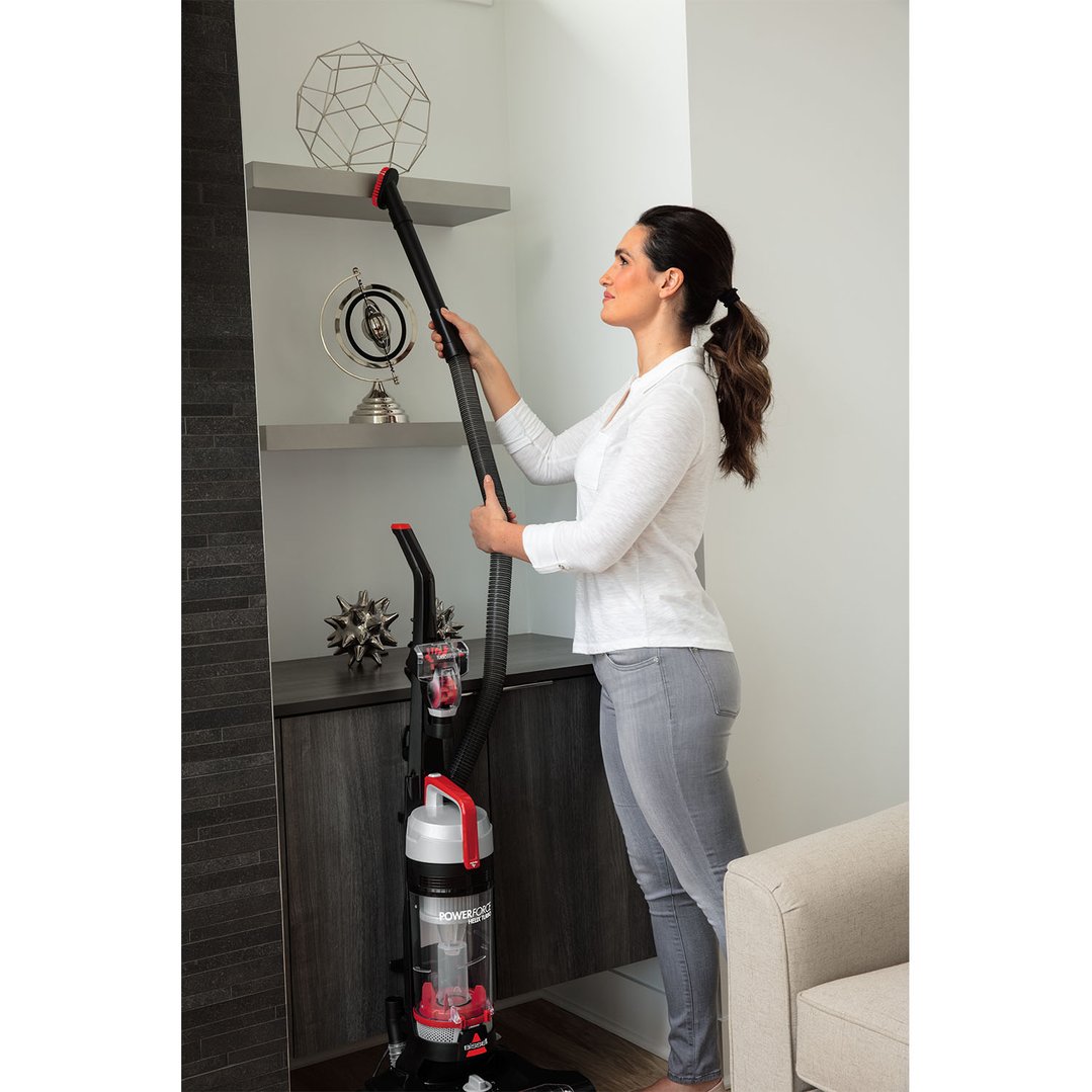 Woman using a BISSELL Powerforce Helix TURBO upright vacuum cleaner to clean shelves