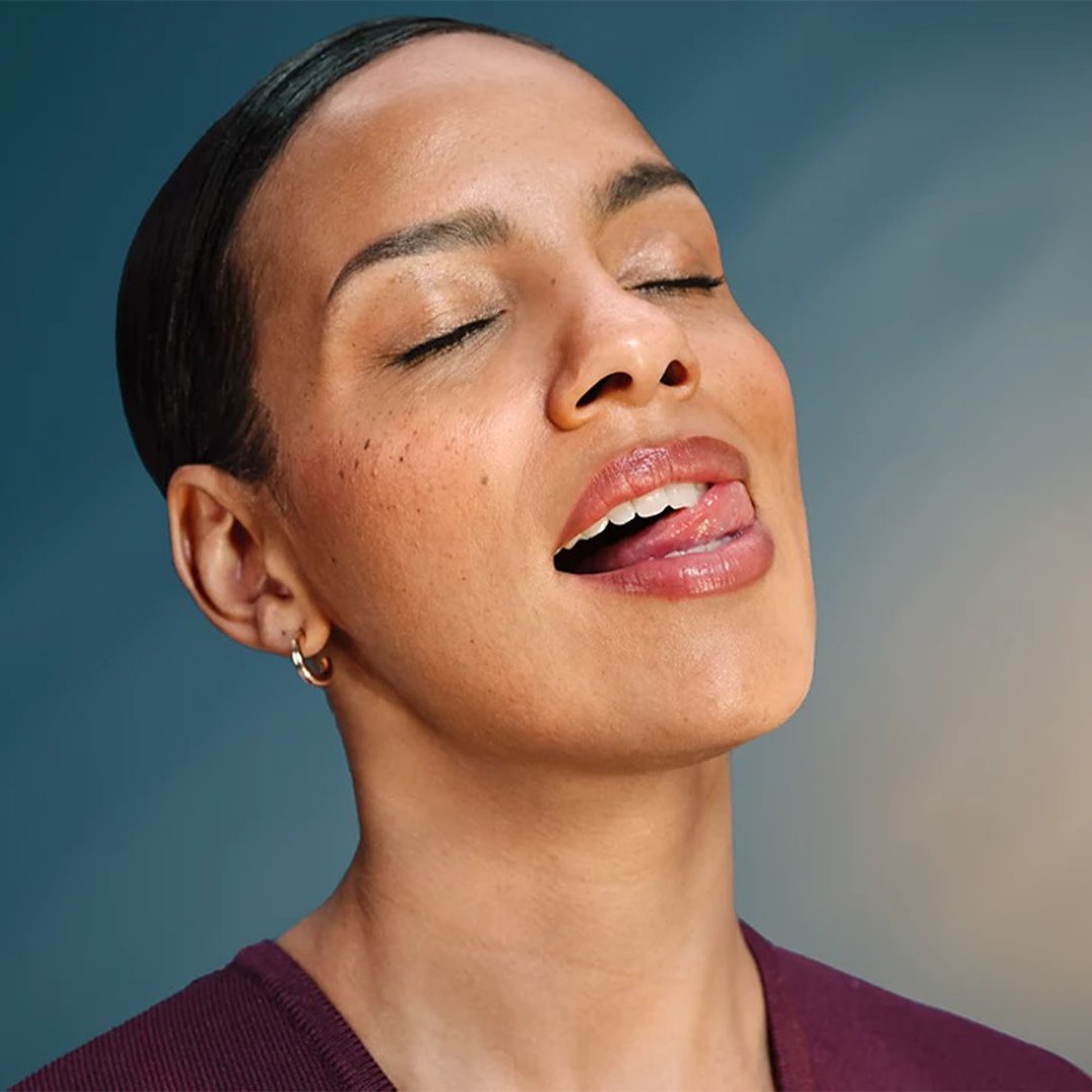 Woman with closed eyes and tongue out, wearing a purple top