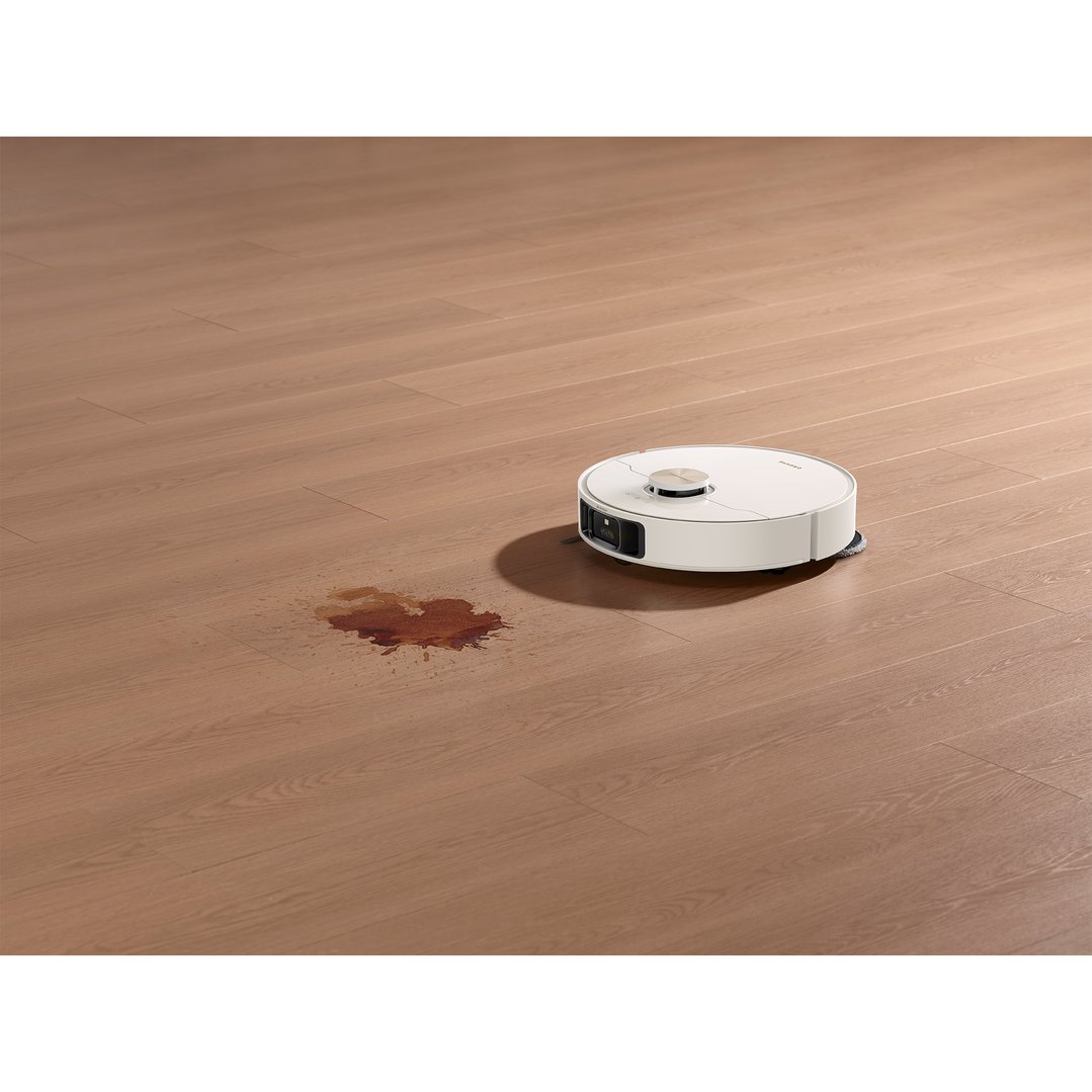 White robot vacuum and mop on a wooden floor next to a spill