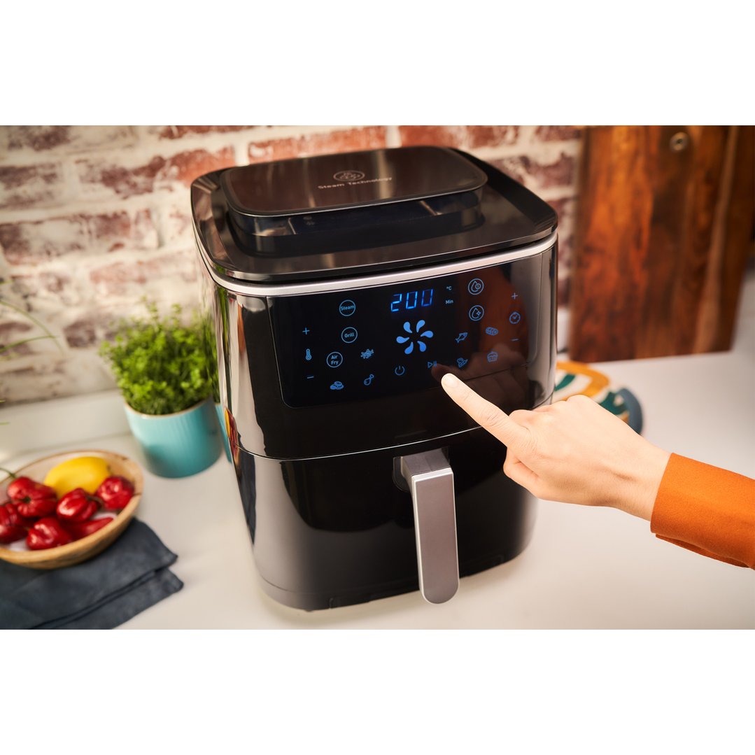 Hand touching the control panel of a black air fryer on a kitchen counter
