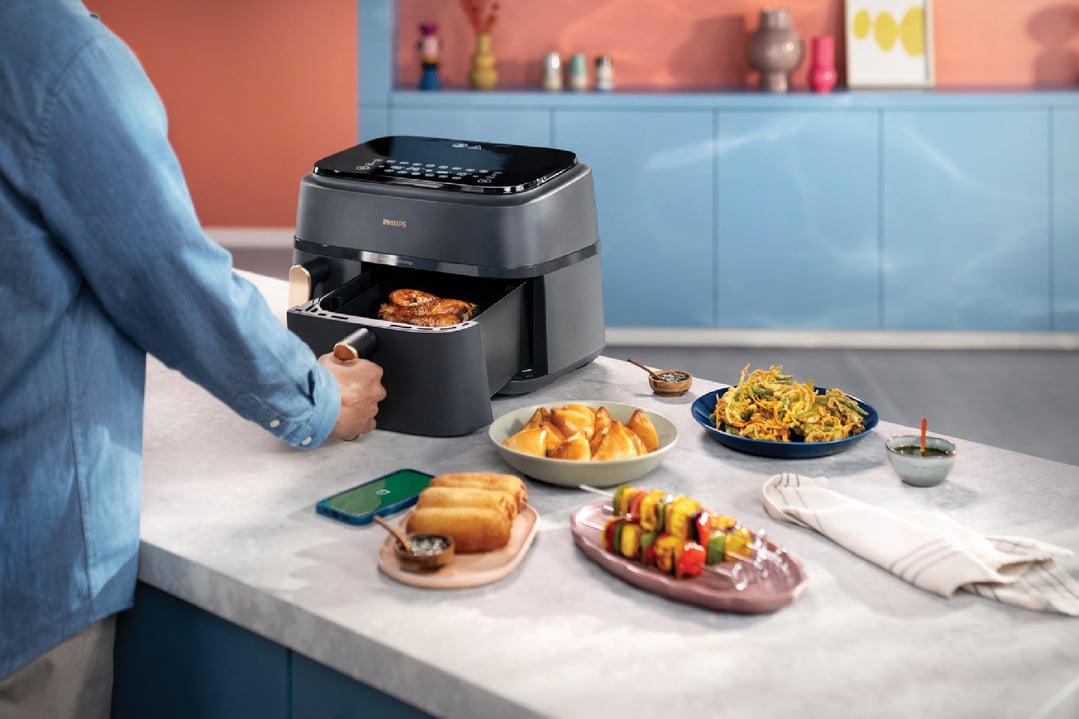 Person pulling out a basket from a Philips airfryer on a kitchen counter