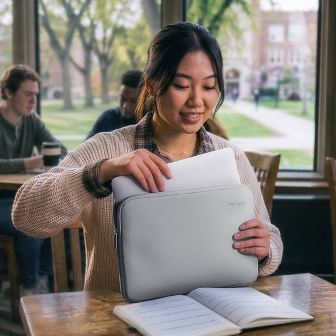 Woman putting a laptop into a grey laptop sleeve at a table