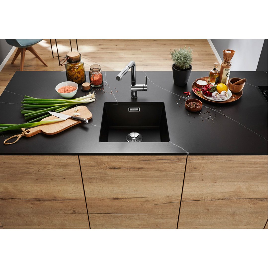 Black sink in a kitchen island with various cooking ingredients and utensils