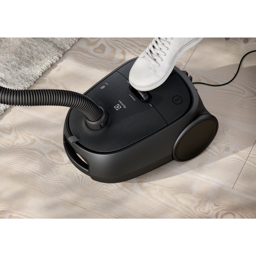 Person's foot on a black Electrolux vacuum cleaner on a wooden floor