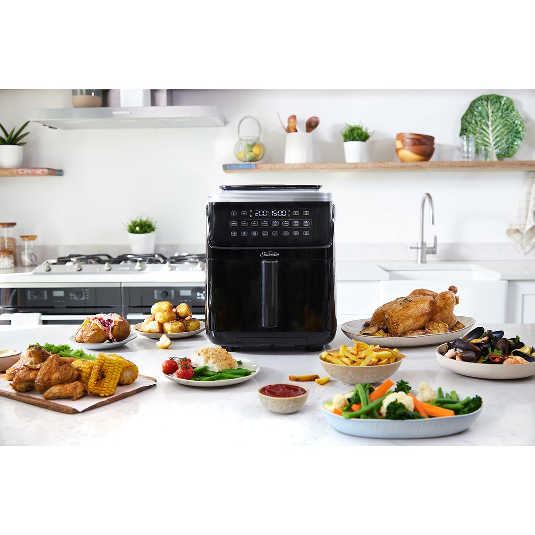 Black Sunbeam SteamFry Air Fryer on a kitchen counter surrounded by cooked food
