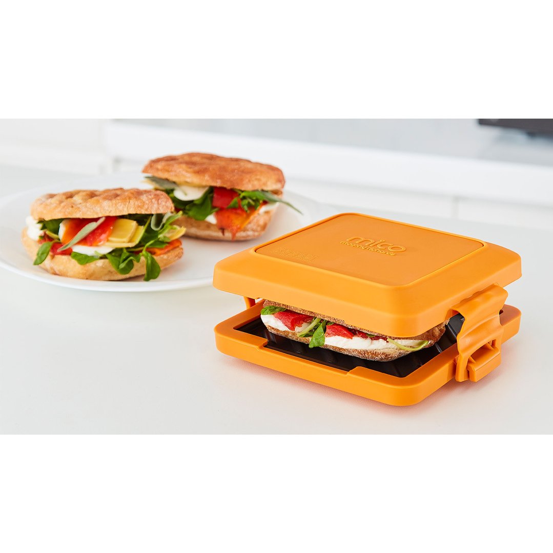 Orange sandwich maker with a sandwich inside, next to two finished sandwiches on a plate