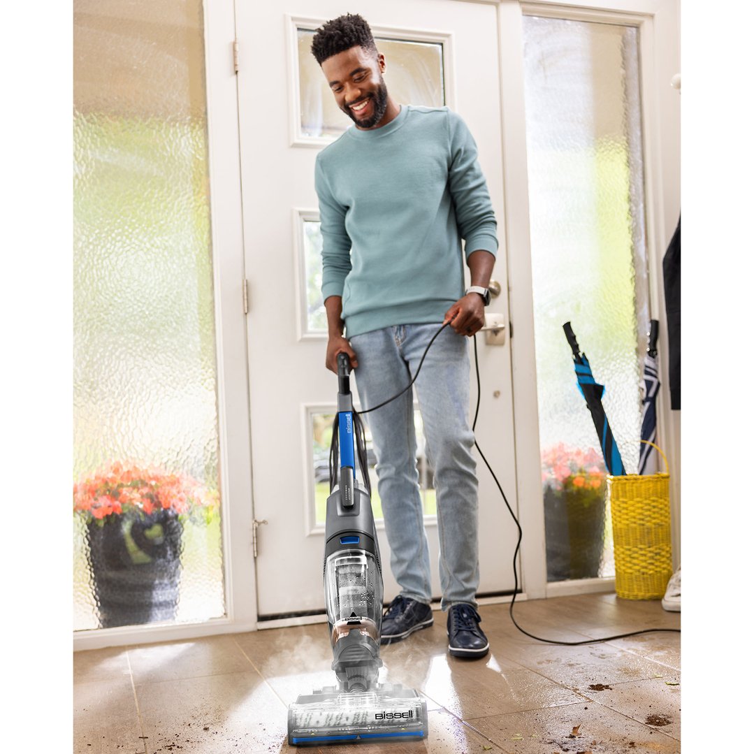 Man using a BISSELL CrossWave HydroSteam vacuum cleaner on a dirty tiled floor