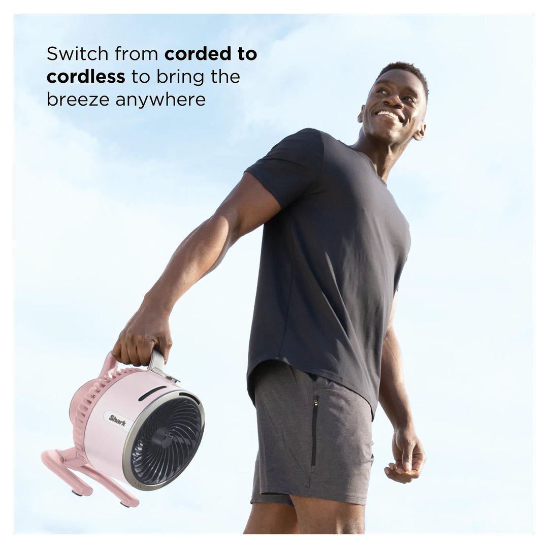 Man holding a pink portable fan outdoors with text overlay about corded to cordless
