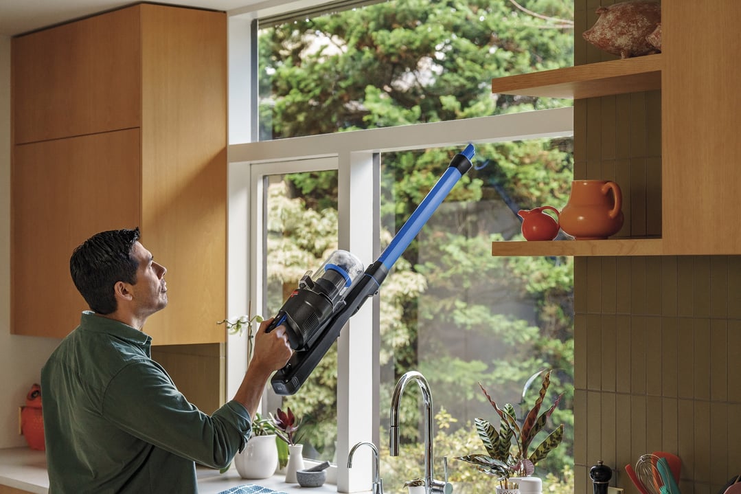 Man using a BISSELL handStickVacuum to clean a high shelf in a kitchen