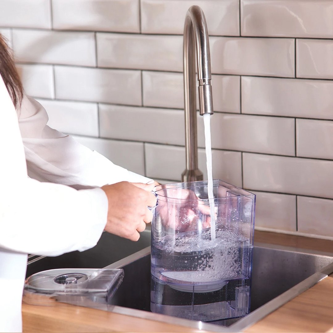 Person filling the AquaStation Hot Water Dispenser with water from a kitchen faucet