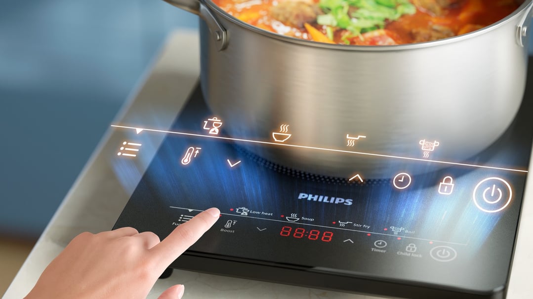Hand touching the control panel of a Philips induction cooker with a pot