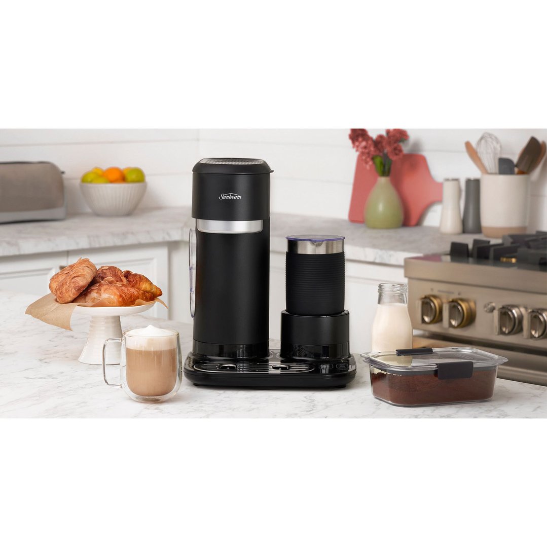 Black coffee machine and milk frother on a kitchen counter with pastries