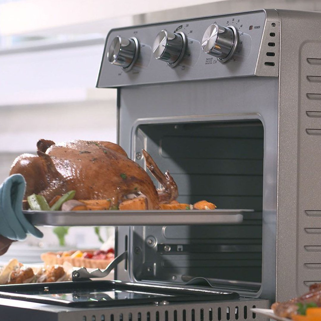 A person placing a roasted chicken with vegetables into a Multi Function Oven + Air Fryer