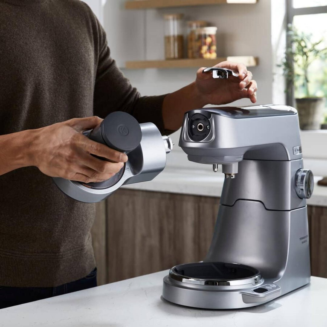 Person attaching a spiralizer attachment to a stand mixer in a kitchen