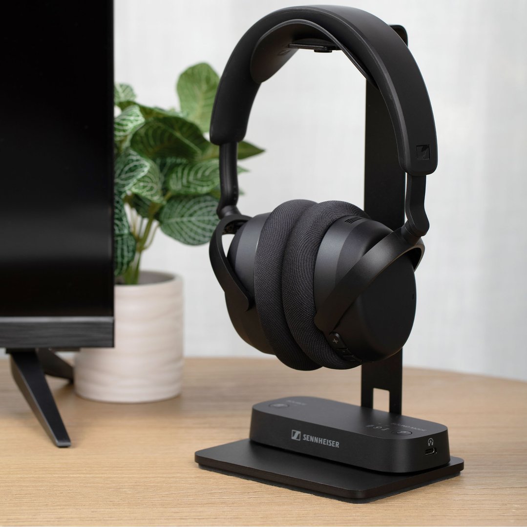 Sennheiser TV headphones on a charging stand next to a TV and plant