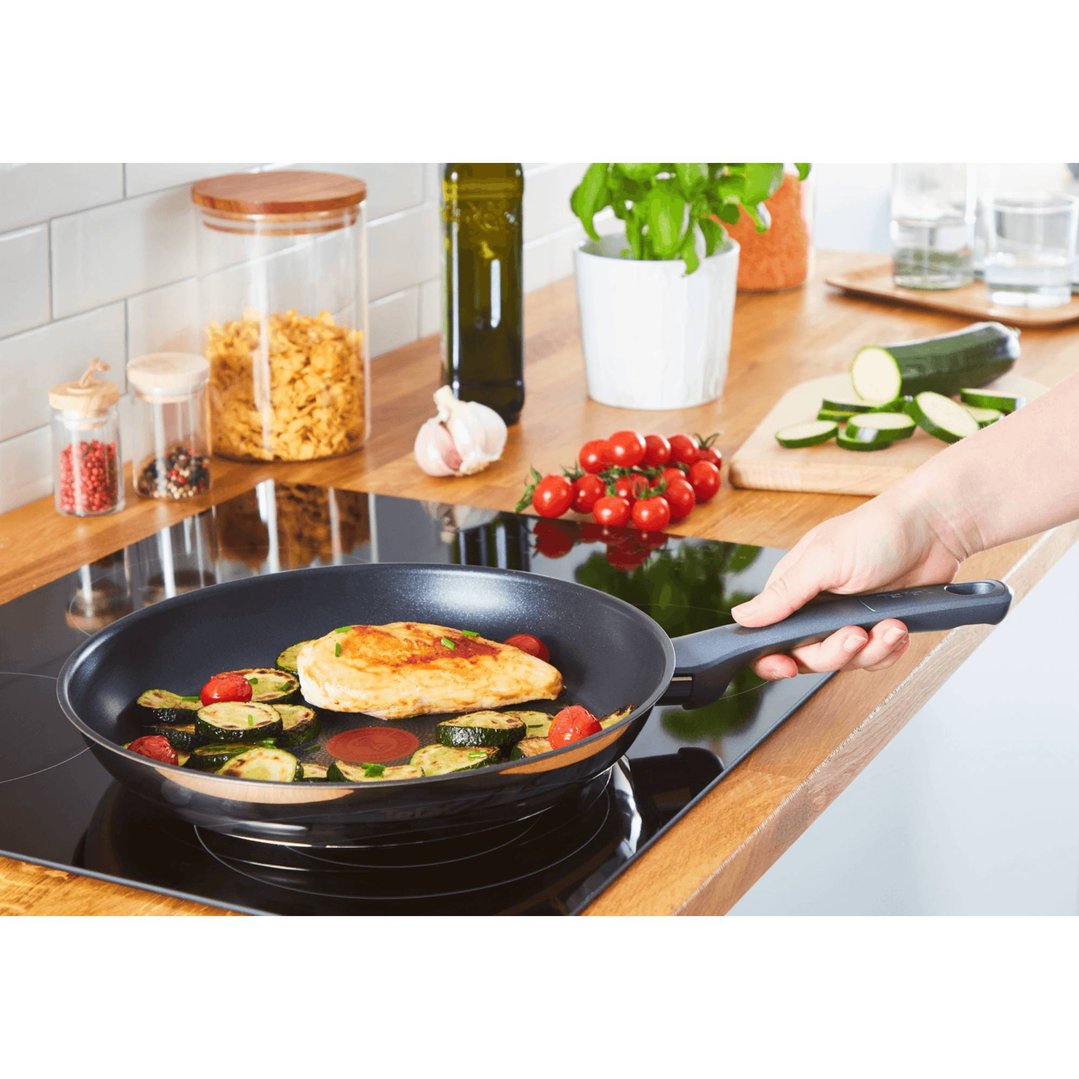 A person cooking chicken and vegetables in a frying pan on an induction cooktop