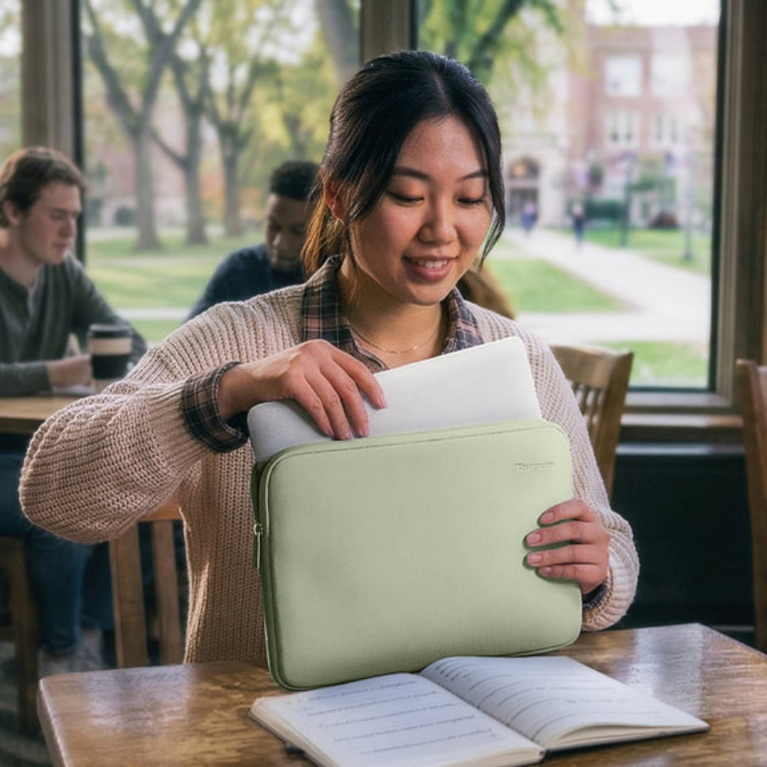 Woman placing a laptop into a green laptop sleeve at a wooden table