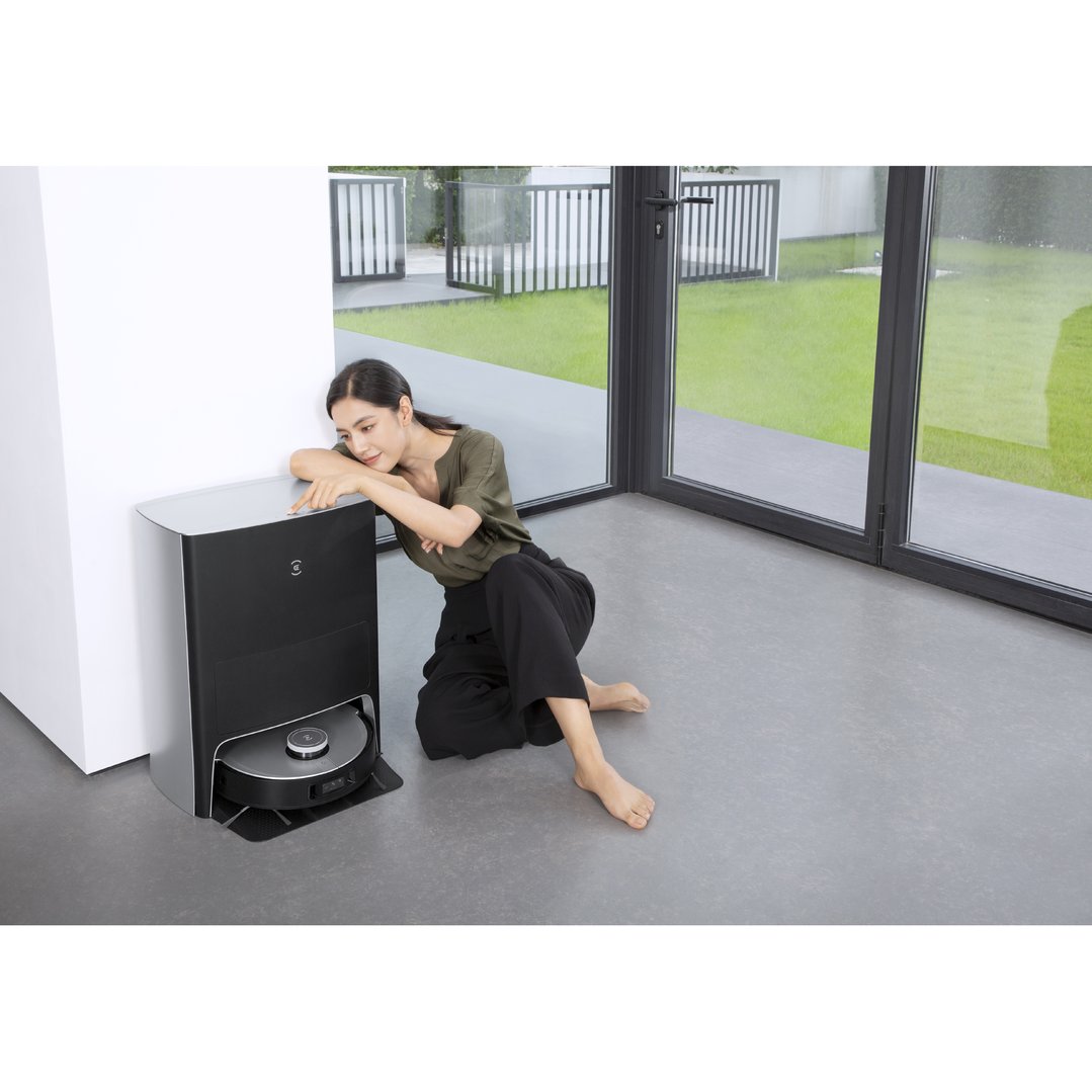 Woman sitting on floor next to a robotic vacuum in a modern room