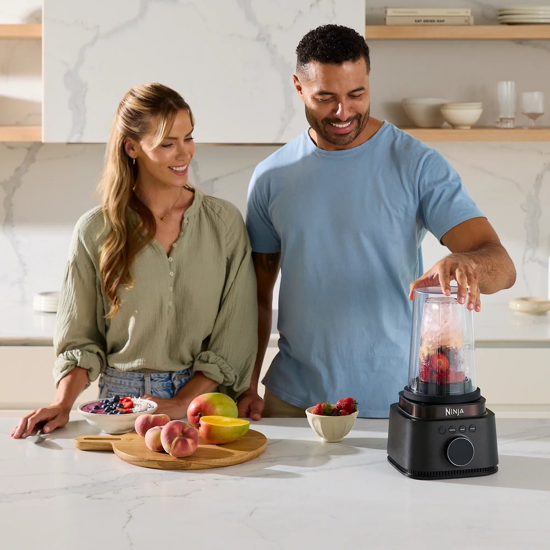 Man and woman preparing fruit for a Ninja blender on a kitchen counter
