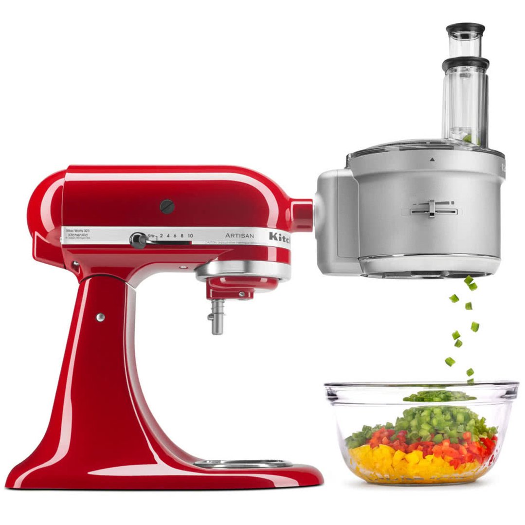 Red stand mixer with food processor attachment chopping vegetables into a glass bowl