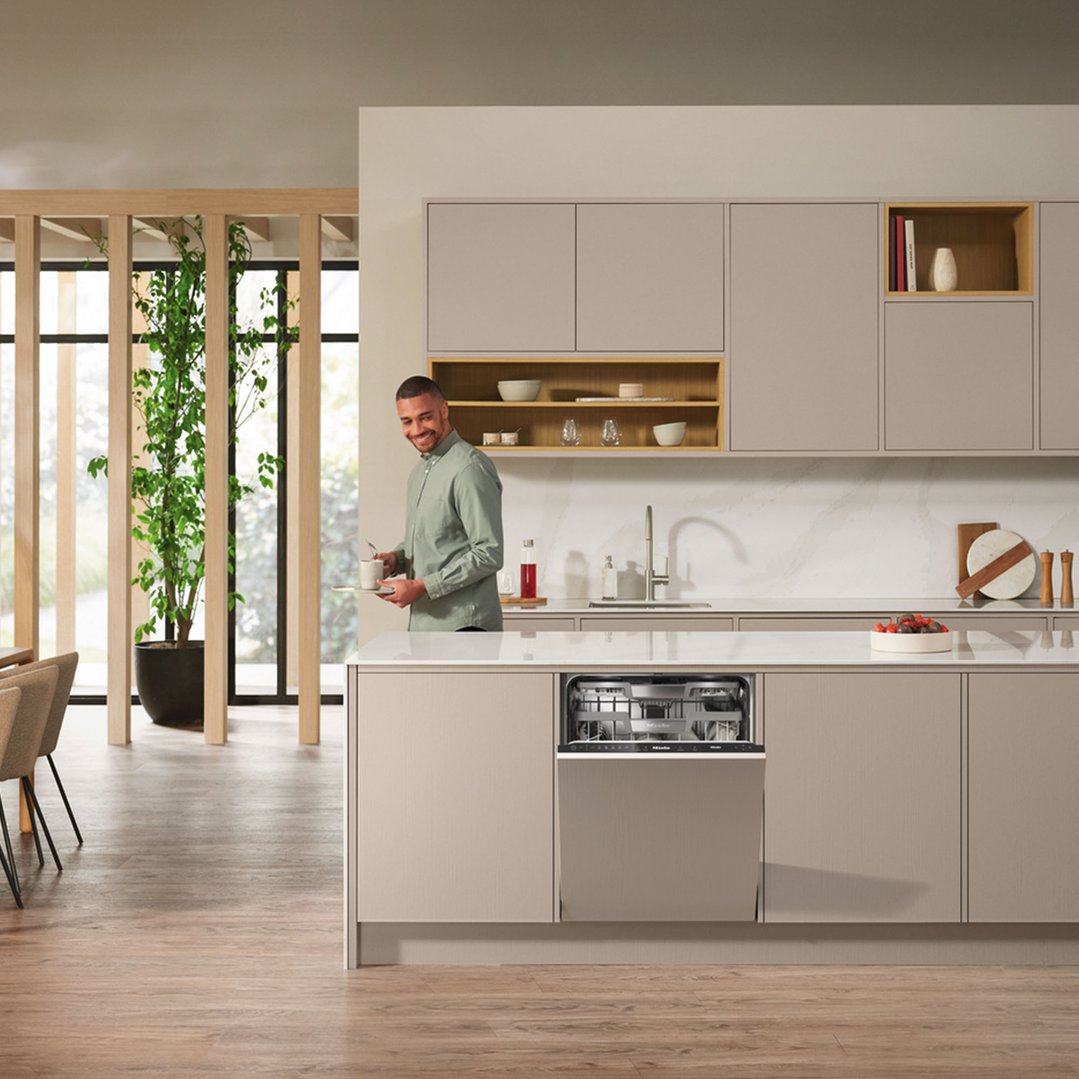 Man holding a tray with a cup in a modern kitchen with a built-in dishwasher